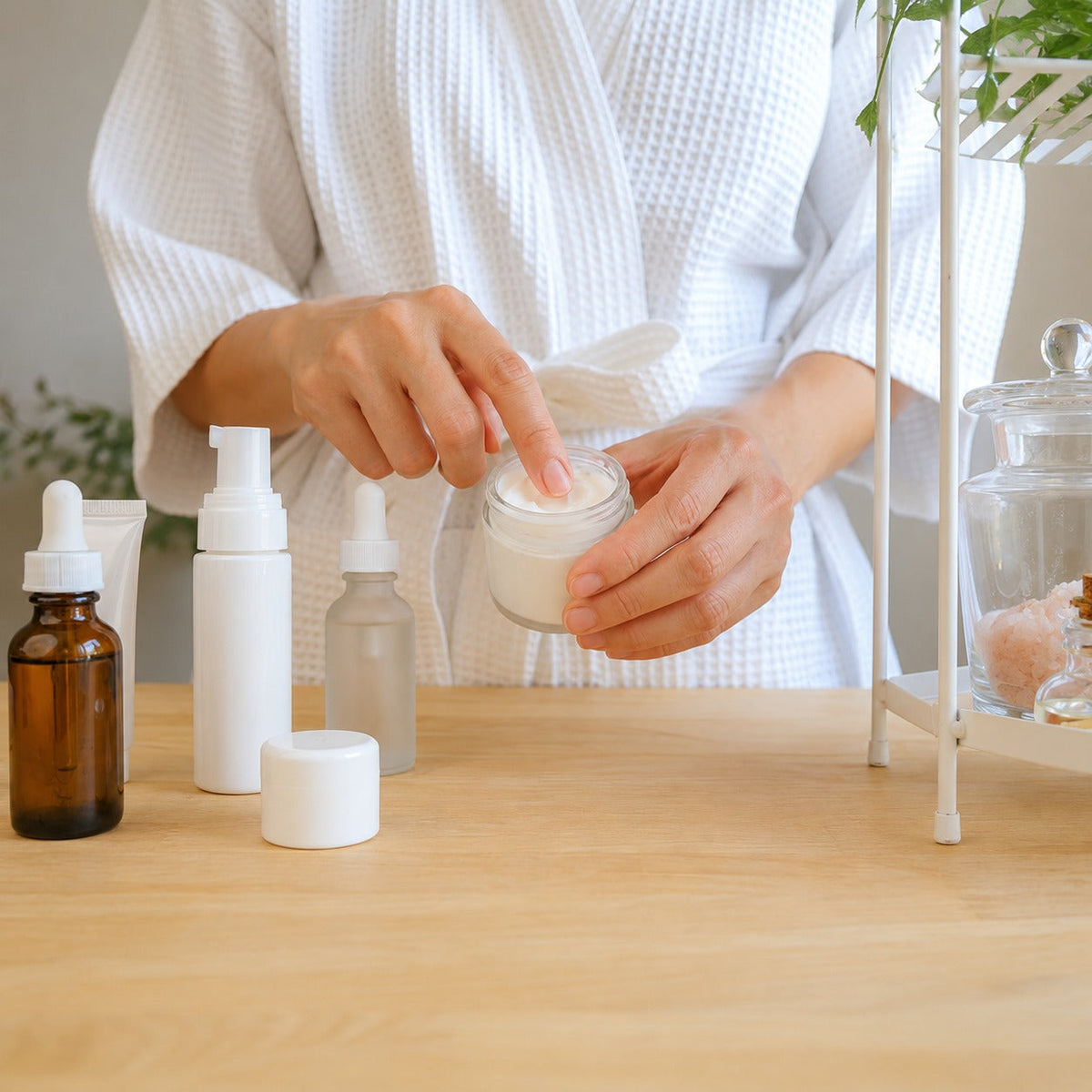 Woman in white robe applying face cream from skincare product collection